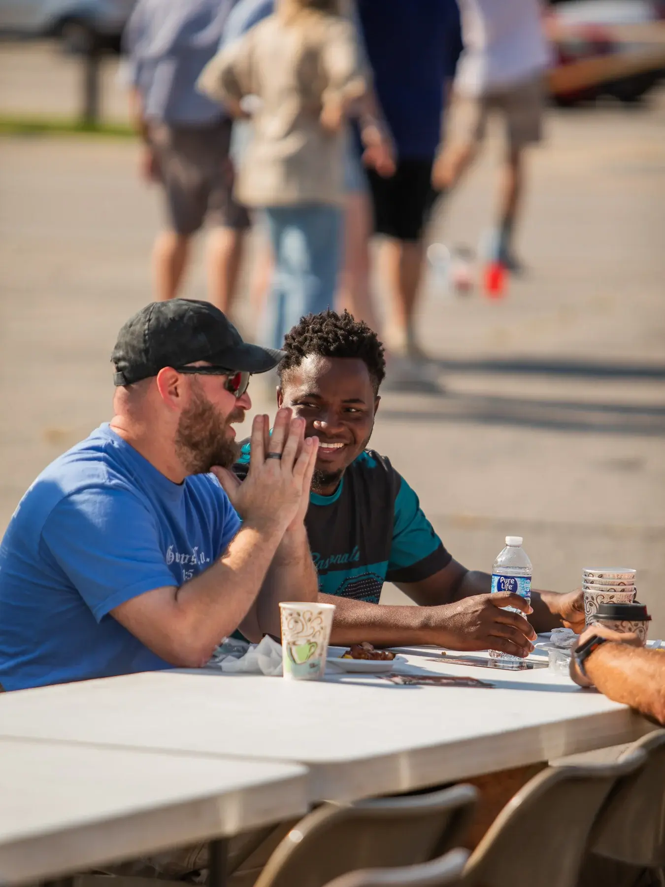 Two neighbors smiling and talking over breakfast at an outdoor table.